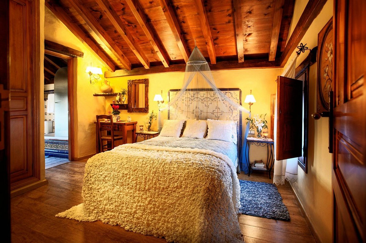 A warm rustic bedroom with exposed beams and a draped bed