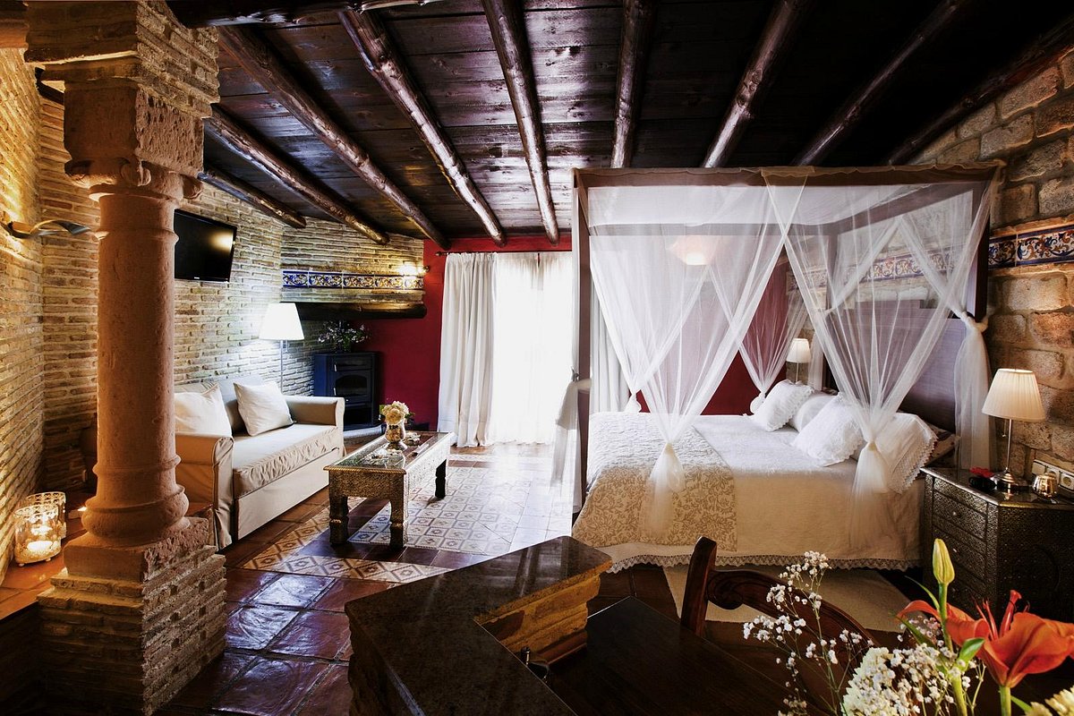 A suite with a four poster bed, stone columns and beamed ceiling